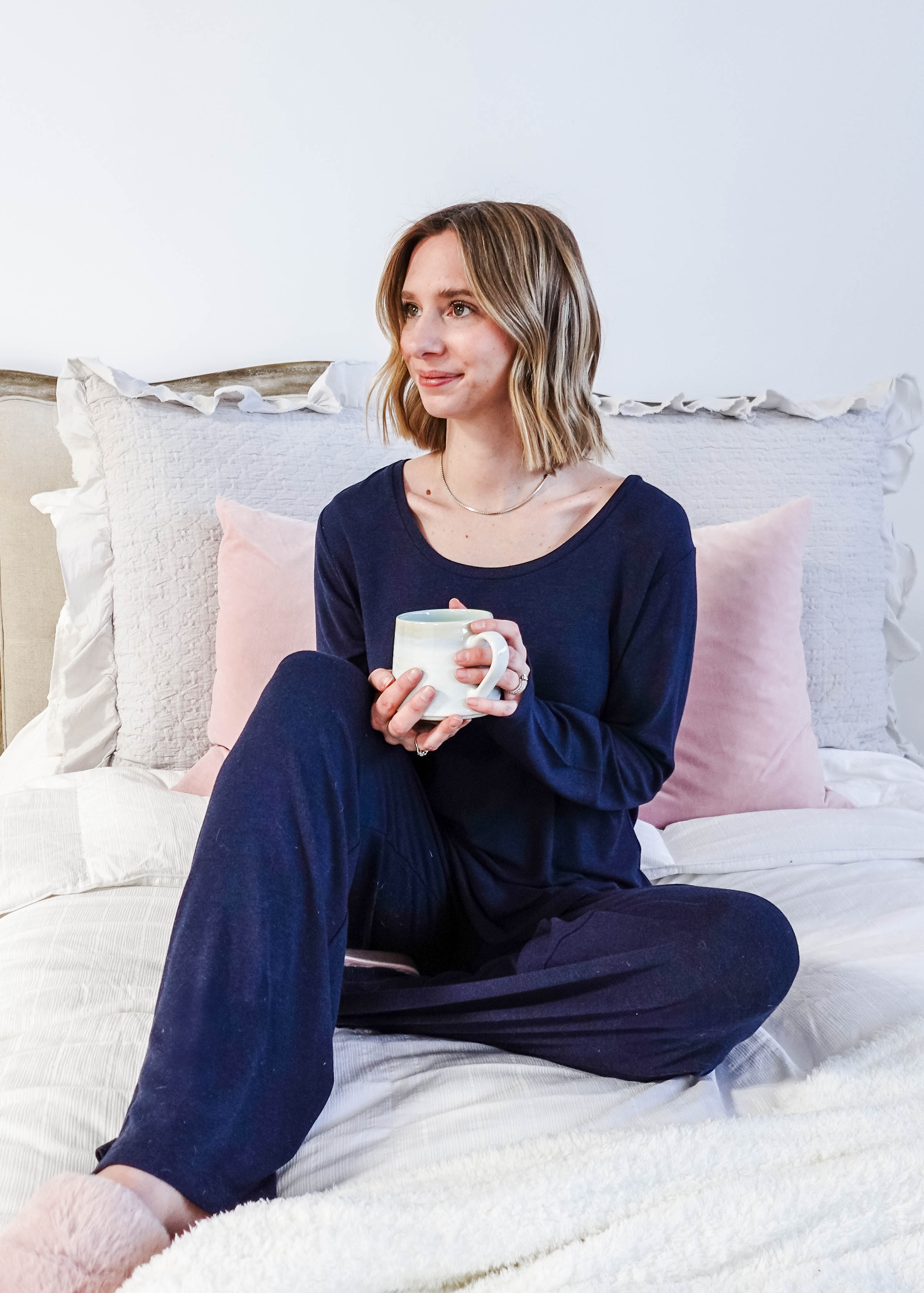 Miranda wearing the Navy Melange Top Straight Pant Knit Lounge Set, highlighting the boat-neck top and flowy trousers - lifestyle shot on bed holding coffee cup