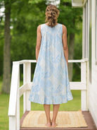 Showing the back of the April Cornell Maddie’s Medley Cotton Nightgown – Embroidered Light Blue Sleeveless Nighty with Button Front. Worn by a model in a cottage/outdoor setting
