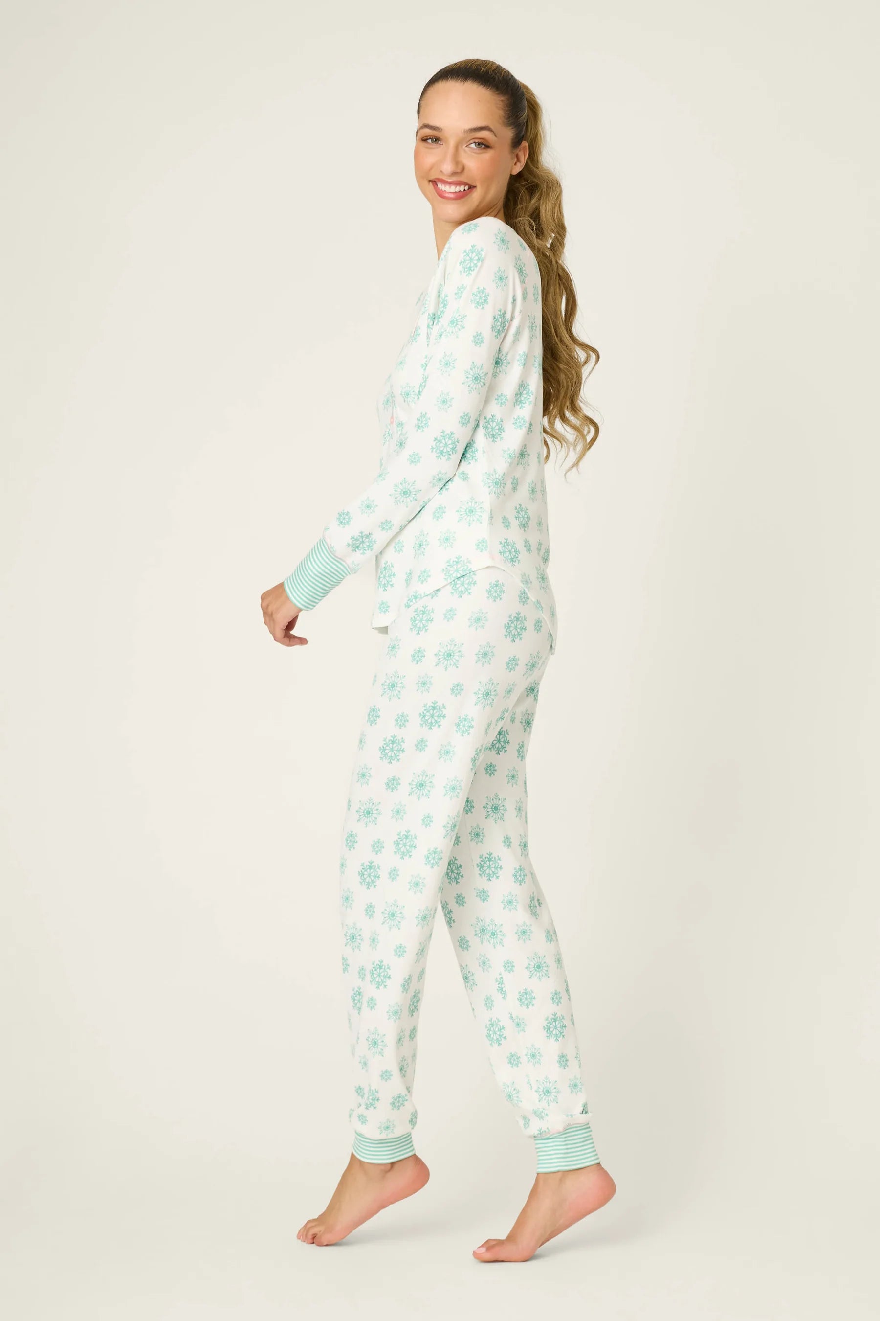 Model (Alexis, 5'8") wearing the PJ Salvage Snowflake Wishes Pointelle PJ Set, showing the ivory V-neck henley top with striped cuffs and jogger pants with a pink tie in the green snowflake print.