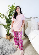 Sydney wearing the Wine Down velvety velour pajama set featuring hot pink wine print pants and a light pink pocket tee.
Showing with shirt untucked