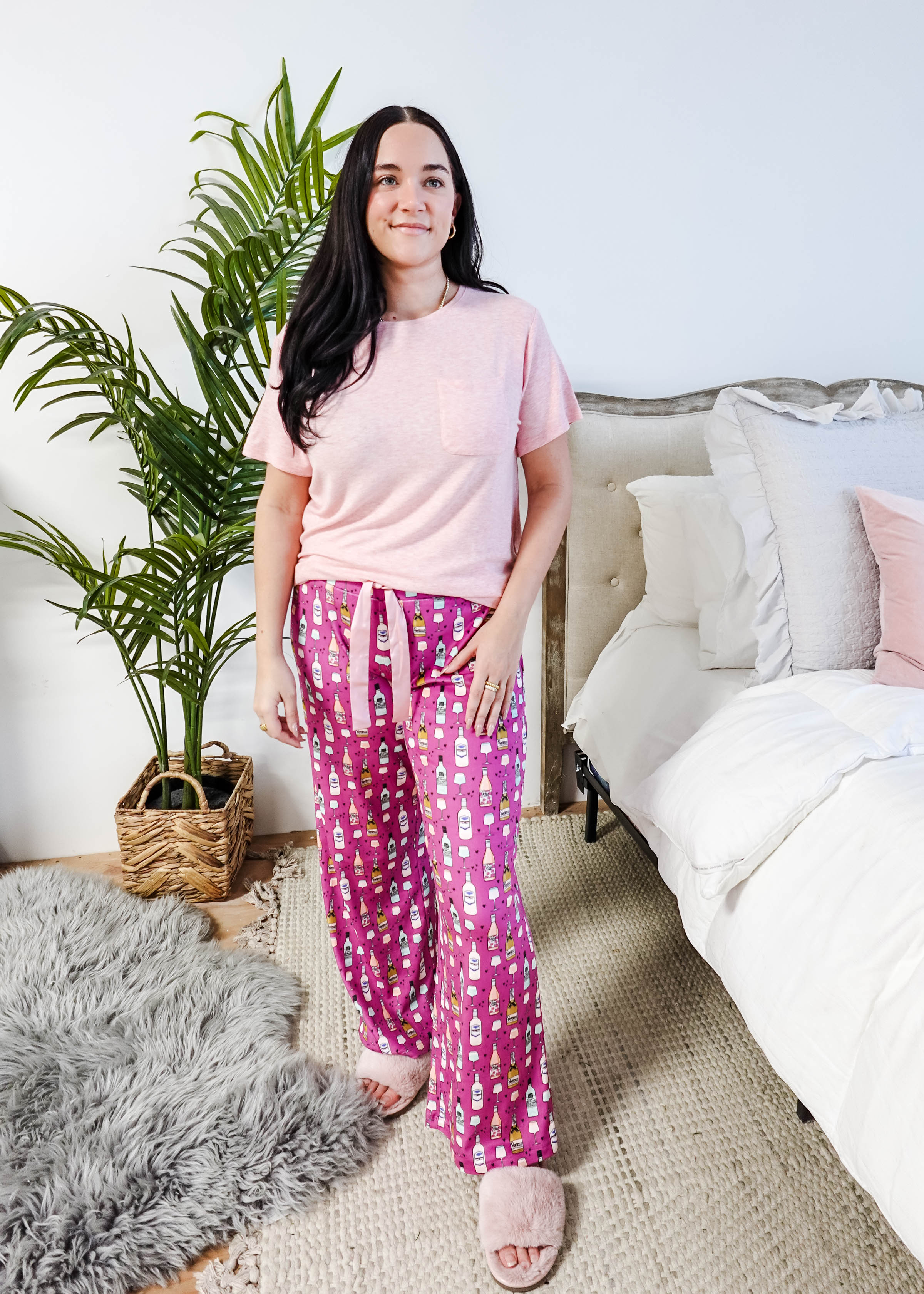Sydney wearing the Wine Down velvety velour pajama set featuring hot pink wine print pants and a light pink pocket tee.
