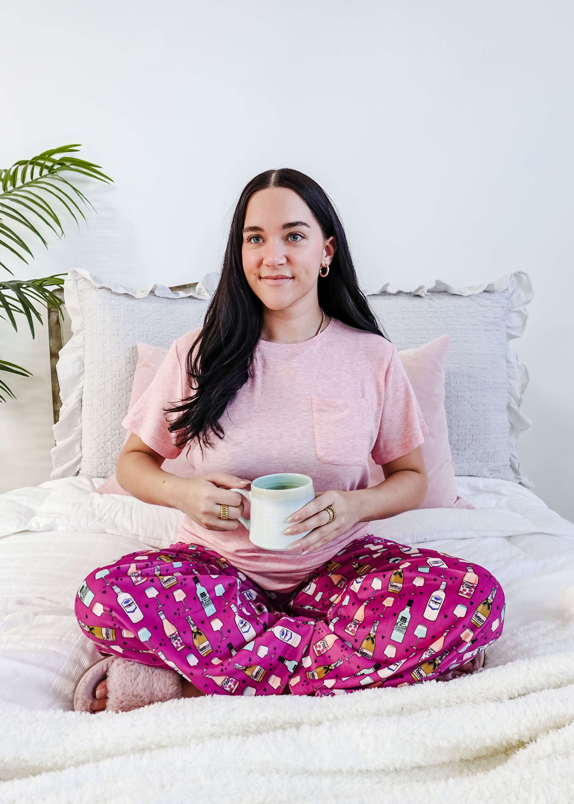 Sydney wearing the Wine Down velvety velour pajama set featuring hot pink wine print pants and a light pink pocket tee.
