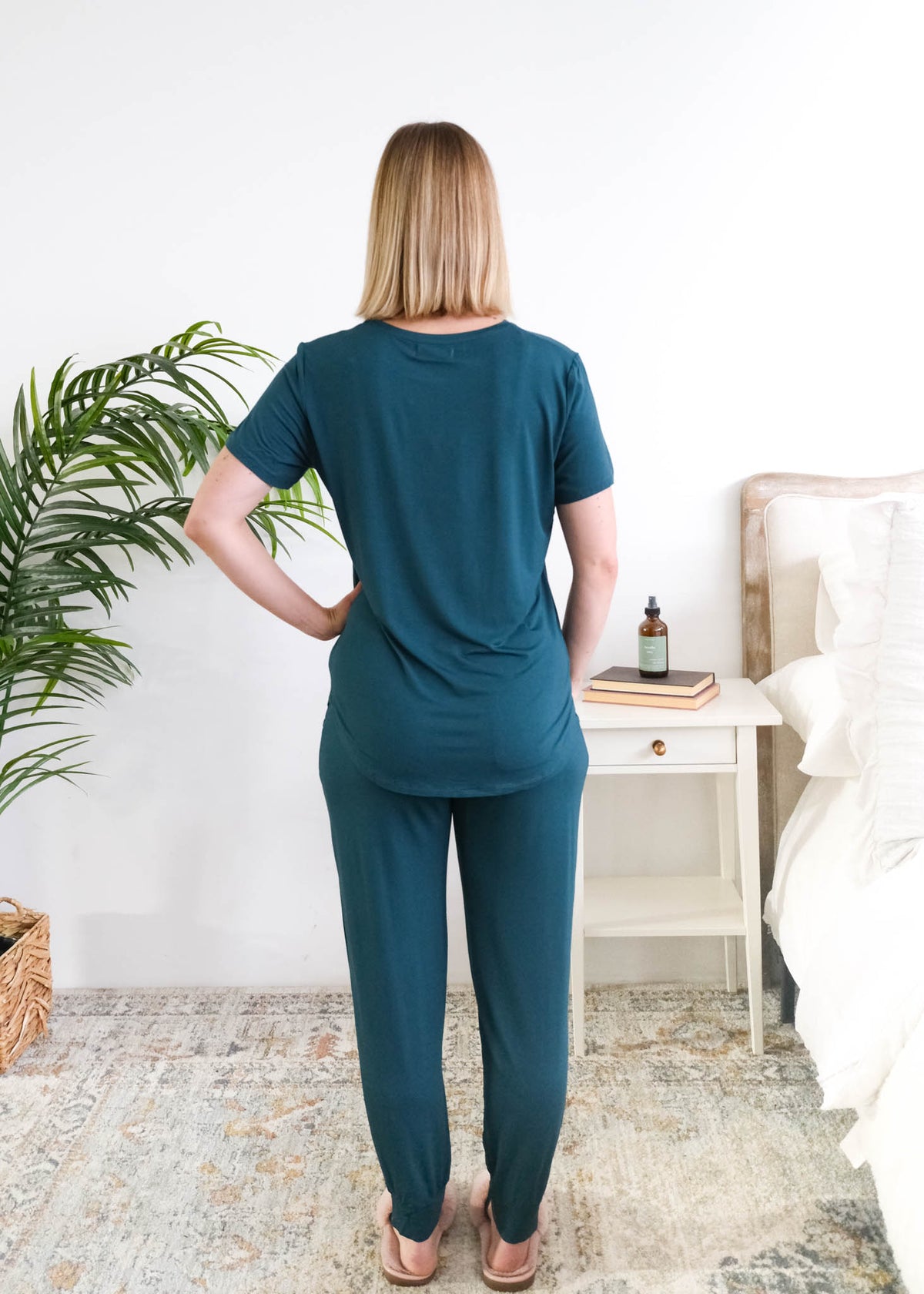 Back view of the Midnight Teal Tee/Jogger PJ Set, showing the relaxed tee length and straight jogger fit. Women is standing in a bedroom. Cloud Nine Pajamas Edmonton