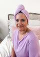 Woman wearing the Remove It Quick Dry Microfiber Hair Towel Wrap in lavender color, smiling on a bed.