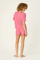 PJ SALVAGE Graphic Print Softee Tee & Short Lounge Set in "Time to Wine Down" rose pink. Model stands against a light background in a back view shot