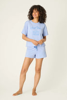 PJ SALVAGE Graphic Print Softee Tee & Short Lounge Set in "Nap Time is my Happy Hour" graphic tee shirt in light blue. Model stands against a light background in a full length shot