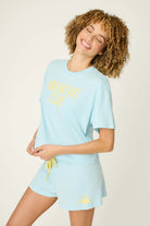 PJ SALVAGE Graphic Print Softee Tee & Short Lounge Set in "Breakfast Club" graphic tee shirt in light blue. Model stands against a light background in a lifestyle profile shot
