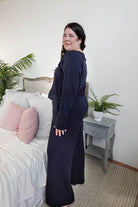 Model wearing Long Sleeve Raw Edge Straight Pant Lounge Set in navy, standing beside a bed with pink pillows and a plant.