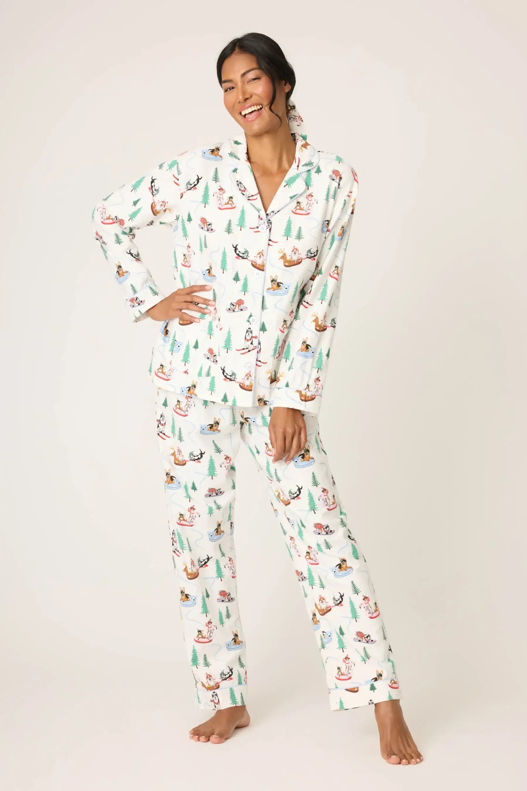 Model Candy wearing the PJ Salvage "Sleigh All Day" 3-Piece Flannel PJ Set in winter white with playful dogs skiing and sledding. She is wearing the button-front top, drawstring pants, and matching headband.