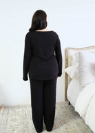 Back view of a black long-sleeve scoop-neck pajama top with a gently curved hem, worn with matching black wide-leg pants that fall straight to the floor. Cloud Nine Pajamas Edmonton. 