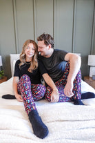 Couple wearing Arcade After Dark Unisex Bamboo Jogger lounging on a bed, showcasing colorful pajama pants.