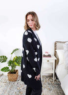 Scarlett Ellie Black Hearts Knit Cardigan | Cloud Nine Pajamas Women standing in a long black open cardigan with white hearts on it in a bedroom 