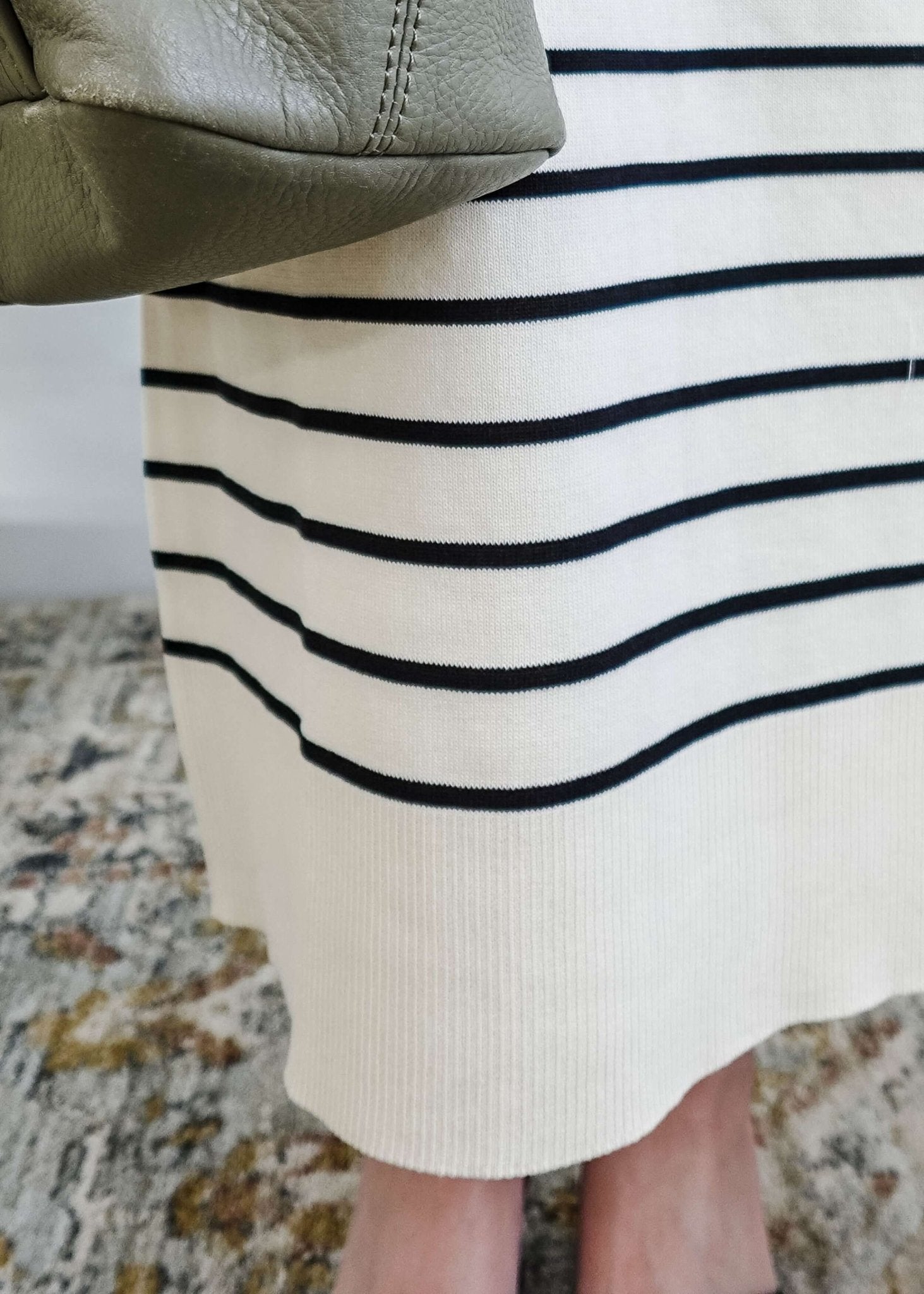 Close-up of a person wearing a white skirt with black stripes and a green purse