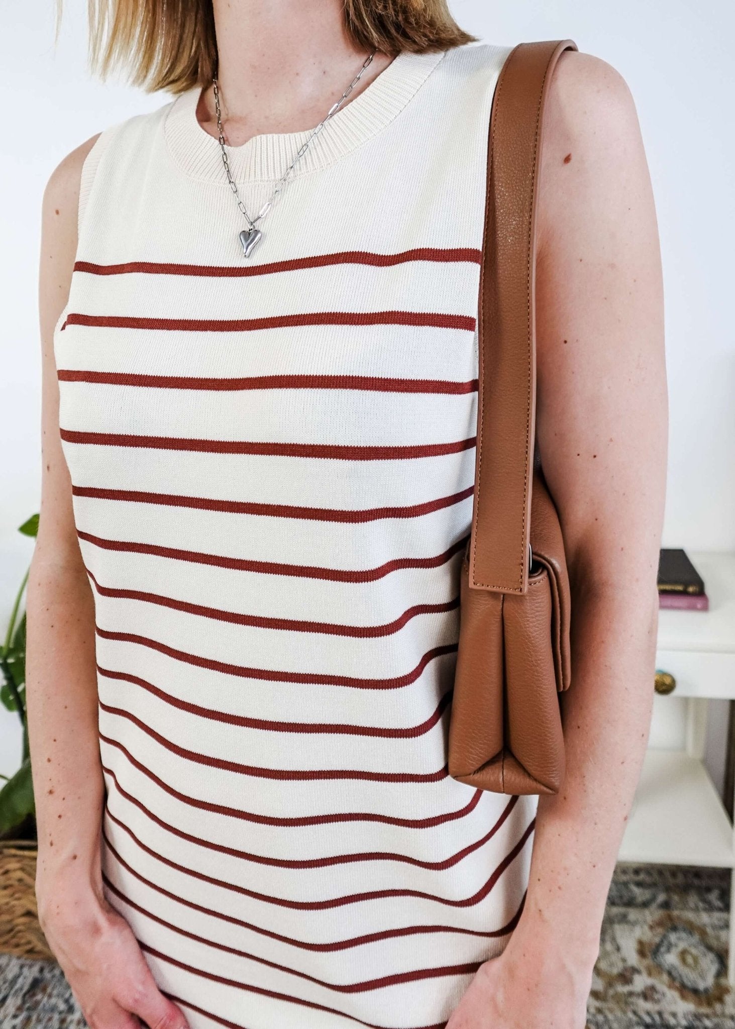 Person wearing a white sleeveless dress with brown stripes and carrying a brown bag.