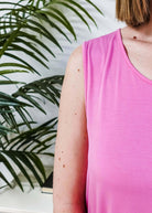 Close-up of a woman wearing the Bubblegum Pink Essential Bamboo Tank Top next to a green plant.