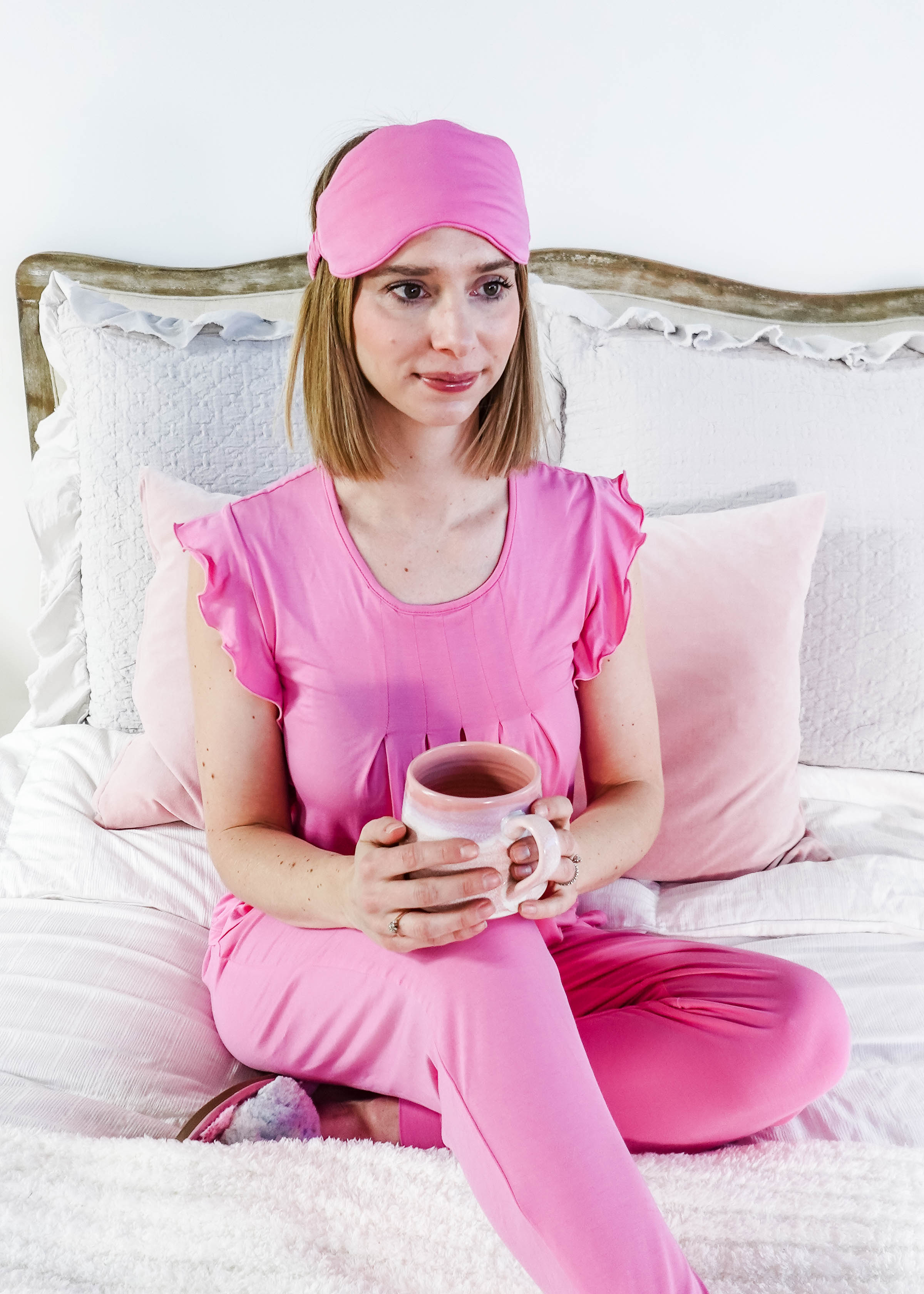 Woman wearing Bubblegum Pink Flutter Top Jogger Bamboo PJ Set, holding a mug, relaxing on a bed.