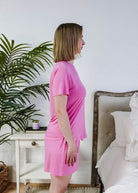 Bubblegum Pink Tee Short Bamboo Pajama Set worn by a woman standing in profile in a cozy bedroom.