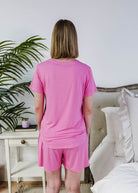 Woman wearing the Bubblegum Pink Tee Short Bamboo Pajama Set, showcasing the back view in a cozy bedroom setting.
