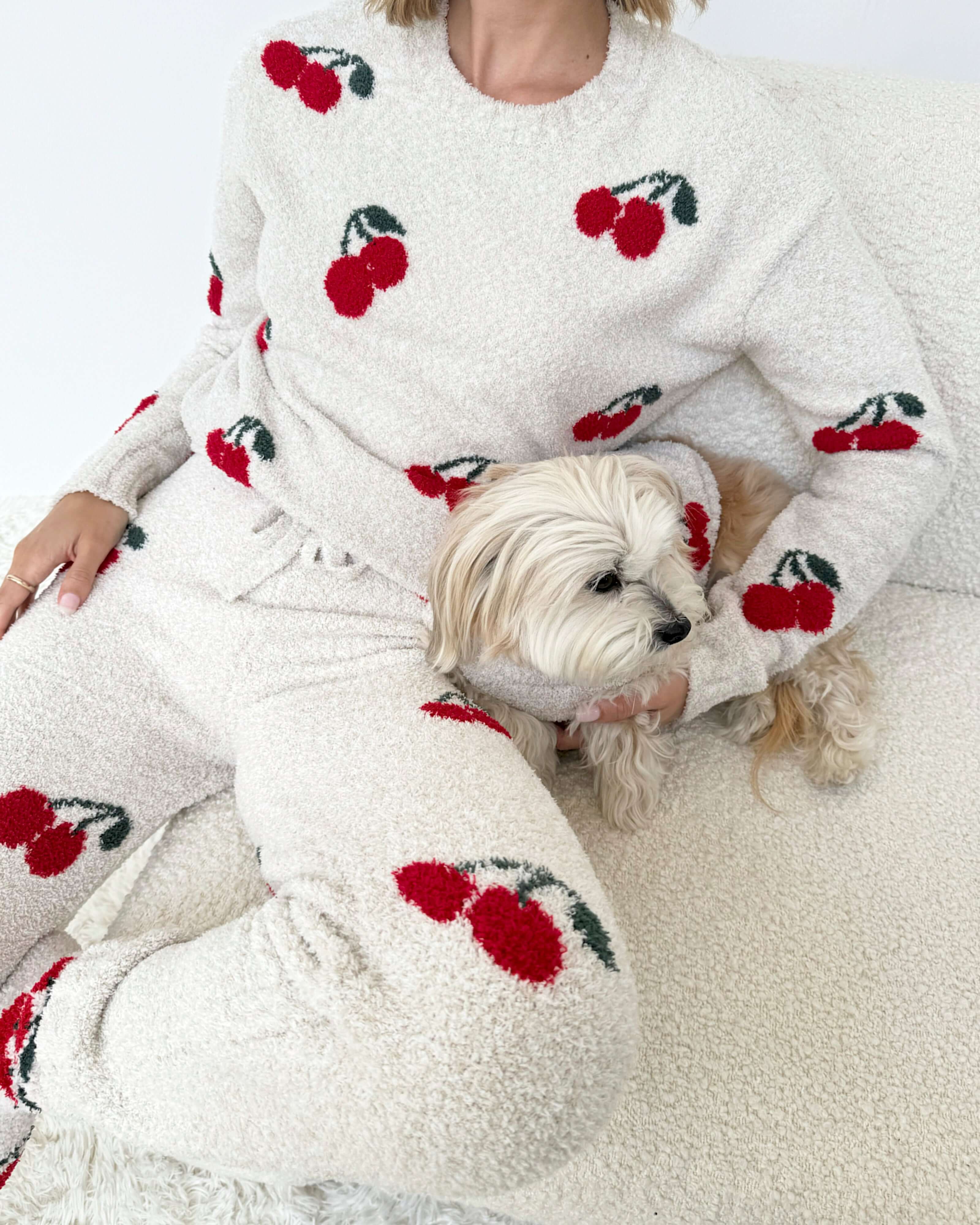 Woman wearing a Cloud-Soft Fuzzy Sweater Pajama Set Splendid with cherry patterns, showcasing cozy loungewear style. Model sitting on a chair.