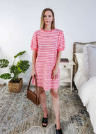 Woman wearing a pink and white striped dress with puffed sleeves in a bedroom setting.
