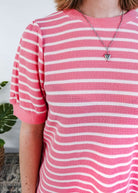Close up of a woman wearing a pink and white striped dress with puffed sleeves in a bedroom setting.