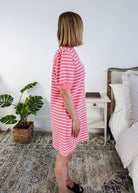 The side of a woman wearing a pink and white striped dress with puffed sleeves in a bedroom setting.