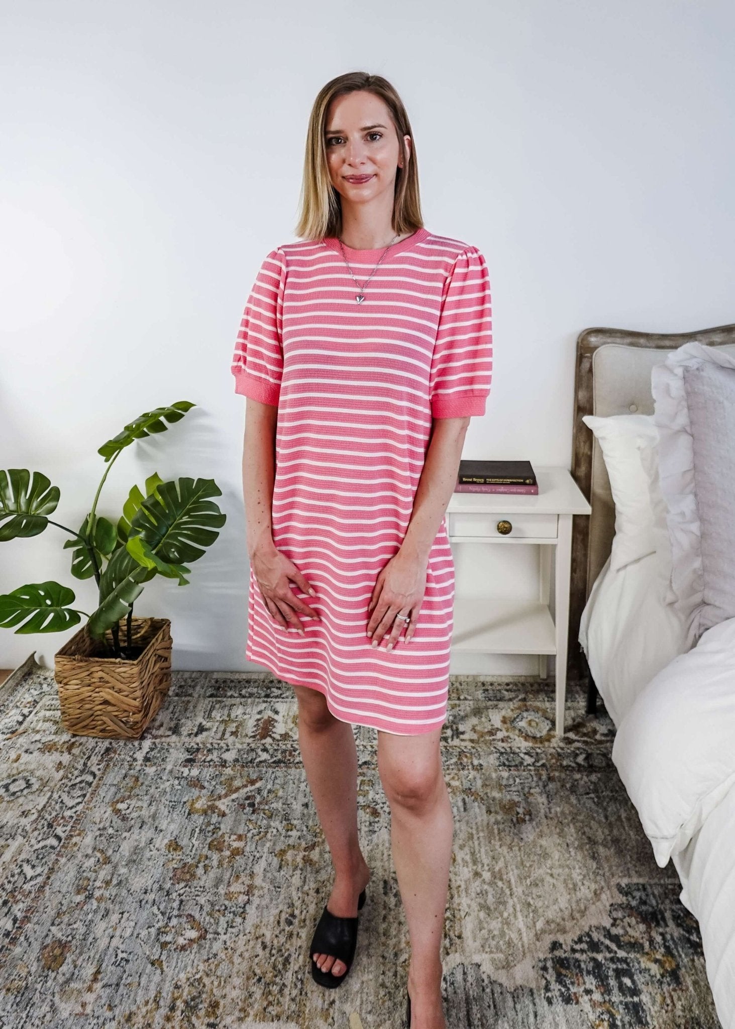 Woman wearing a pink and white striped dress with puffed sleeves in a bedroom setting.