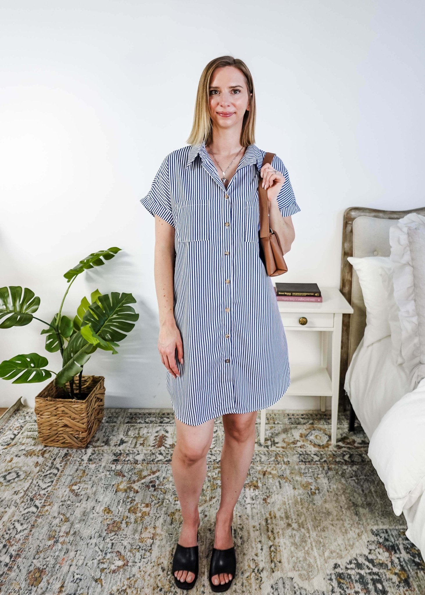Woman in a blue and white striped dress holding a brown bag in a bedroom setting. Scarlett Ellie Collared Button-Up Short Sleeve Dress | Cloud Nine Pajamas