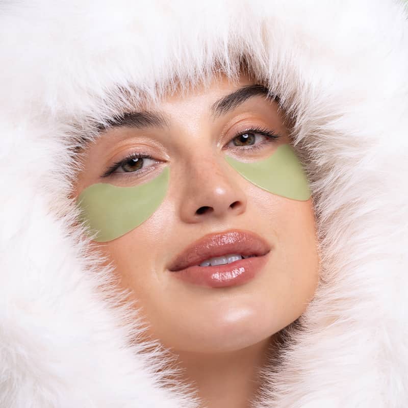Woman wearing green eye patches with a white hood, Patchology Cool Crush Hydrogel Eye Patch single pair depuffing treatment