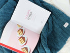 Open book with dessert illustration on a teal blanket