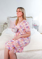 Model wearing the Dream in Blooms V Neck Nightshirt With Pockets, sitting on a bed holding a cup.