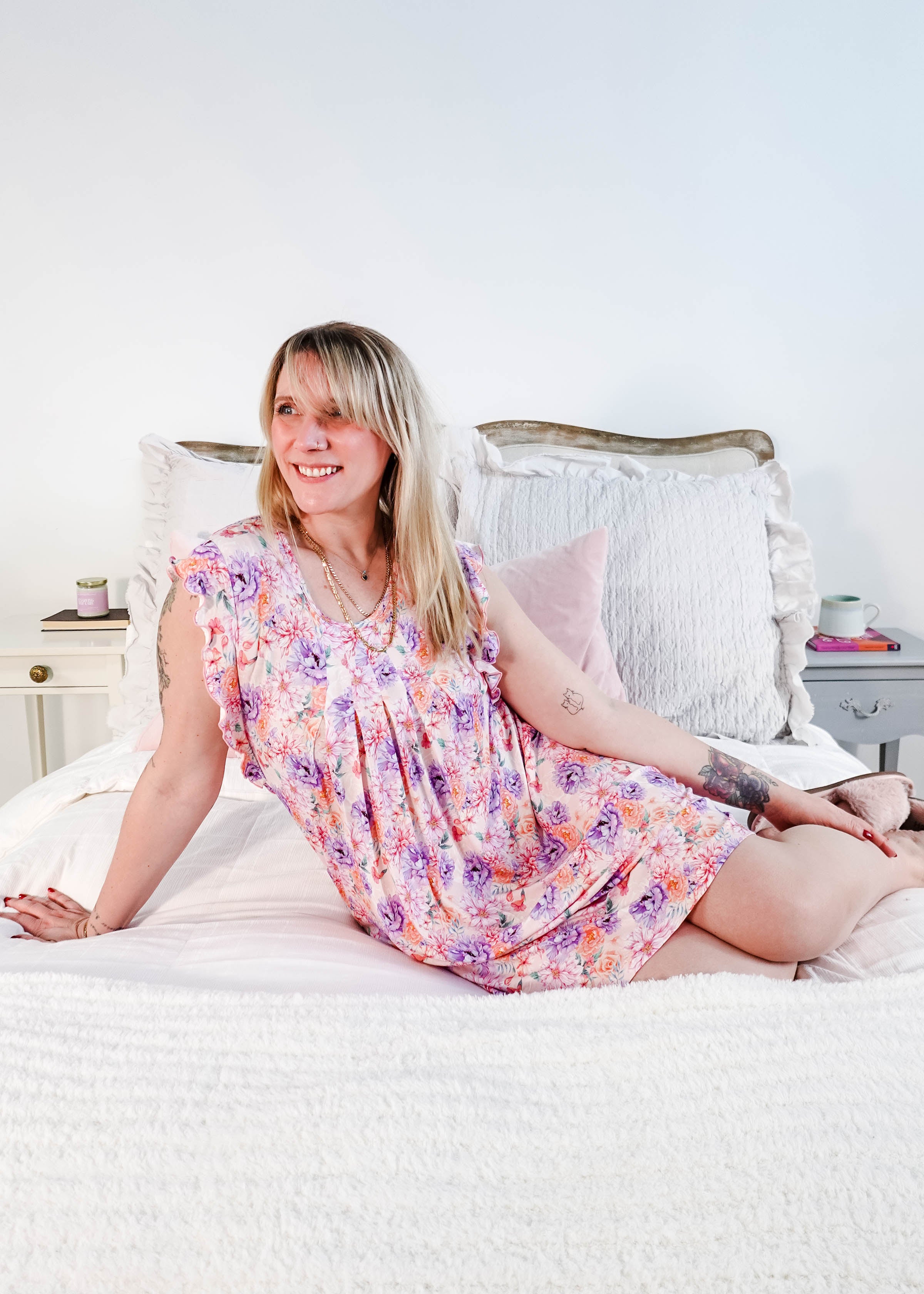 Dream In Blooms Flutter Bamboo Nightgown displayed on a smiling woman sitting on a bed, showcasing romantic sleepwear.