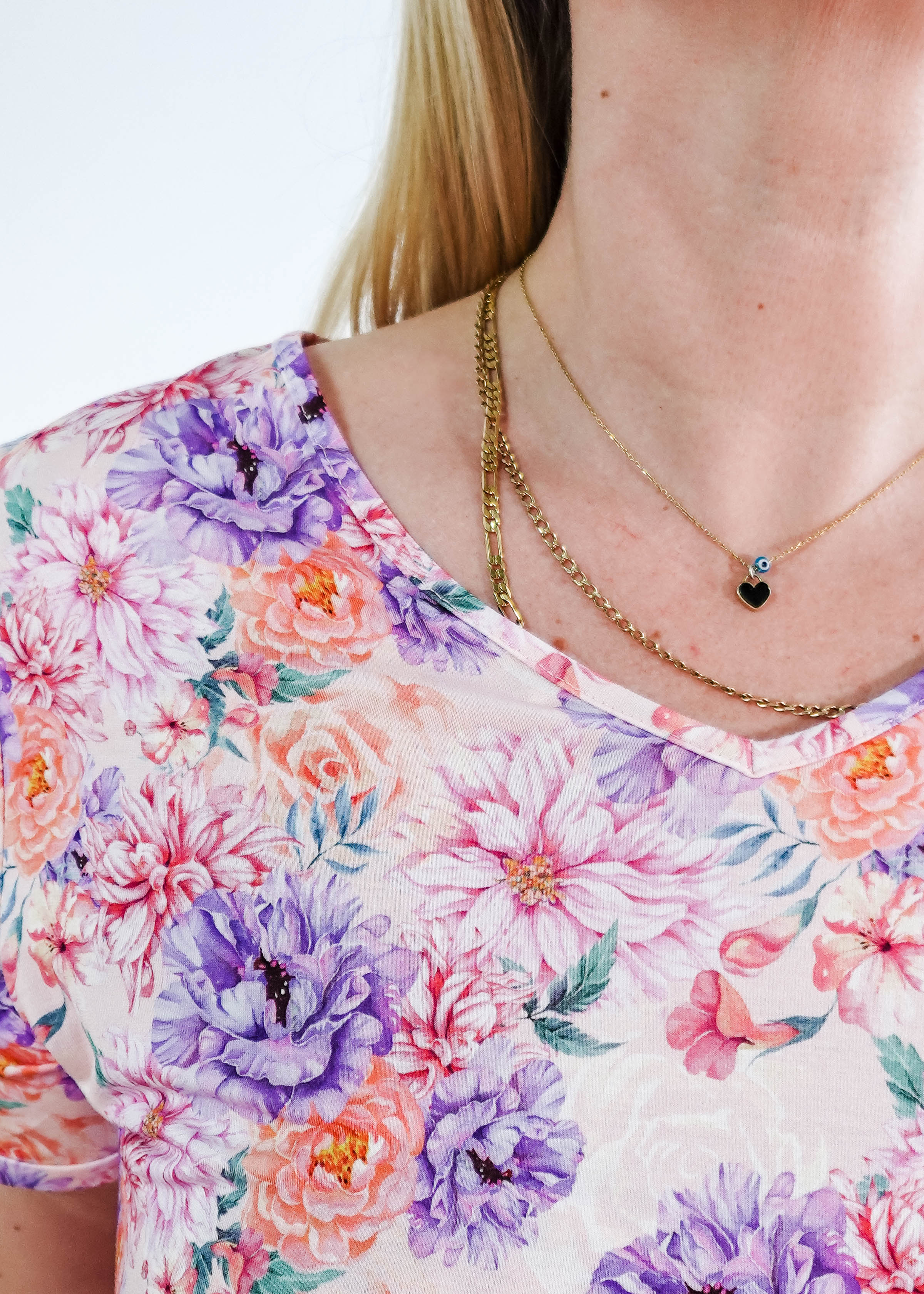 Close-up of a woman wearing the Dream in Blooms V Neck Nightshirt With Pockets featuring vibrant floral patterns and layered necklaces.