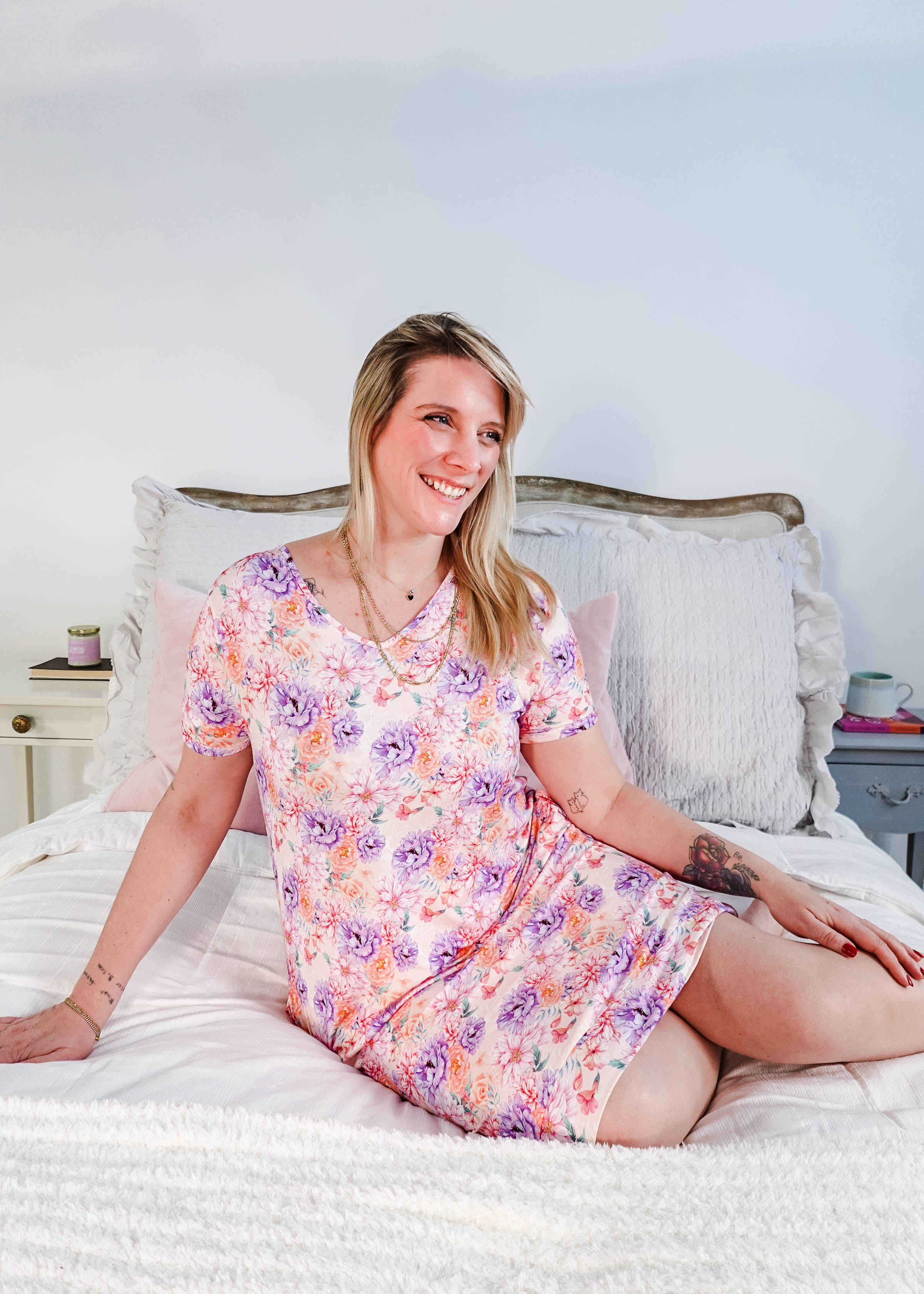 Dream in Blooms V Neck Nightshirt With Pockets worn by a woman sitting on a bed, featuring a floral design.