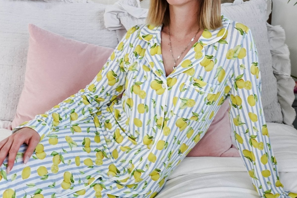 Woman wearing a lemon-patterned dress sitting on a couch with pink pillows.