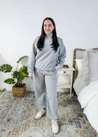 Woman wearing a grey sweatsuit standing in a bedroom with a plant and bed in the background, Scarlett Ellie Half-Zip Sweatsuit Set | Cloud Nine Pajamas