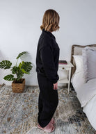 Woman wearing a black sweatsuit standing in a bedroom with a plant and bed in the background, Scarlett Ellie Half-Zip Sweatsuit Set | Cloud Nine Pajamas
