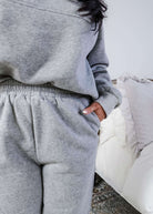 Woman wearing a grey sweatsuit standing in a bedroom with a plant and bed in the background, Scarlett Ellie Half-Zip Sweatsuit Set | Cloud Nine Pajamas