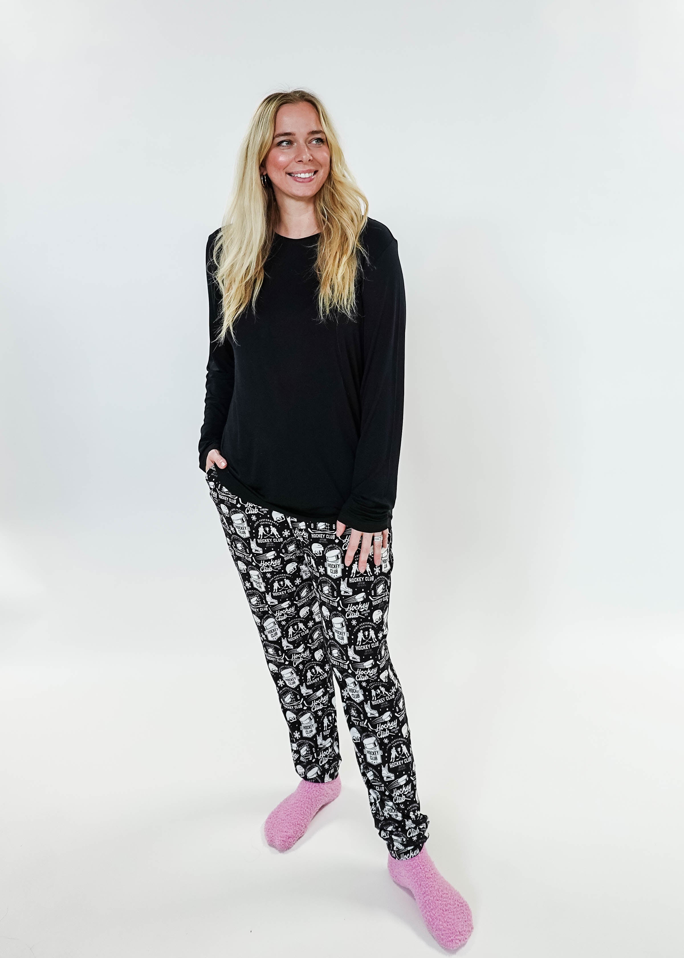 Woman wearing He Scores Hockey Print Unisex Bamboo Jogger with a black long sleeve top and pink slippers.