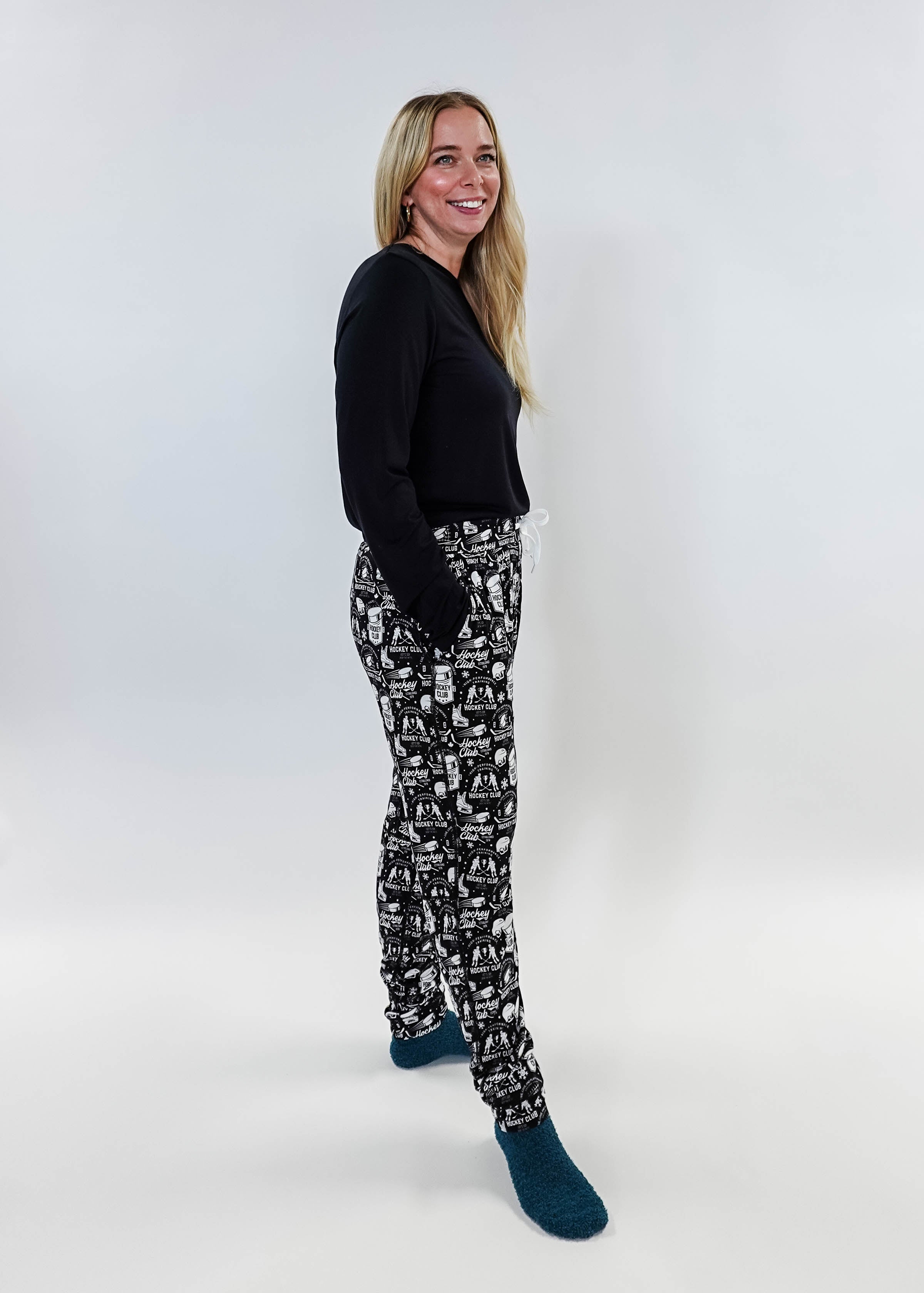 Female model wearing He Scores Hockey Print Unisex Bamboo Jogger with a black long-sleeve top and blue socks.