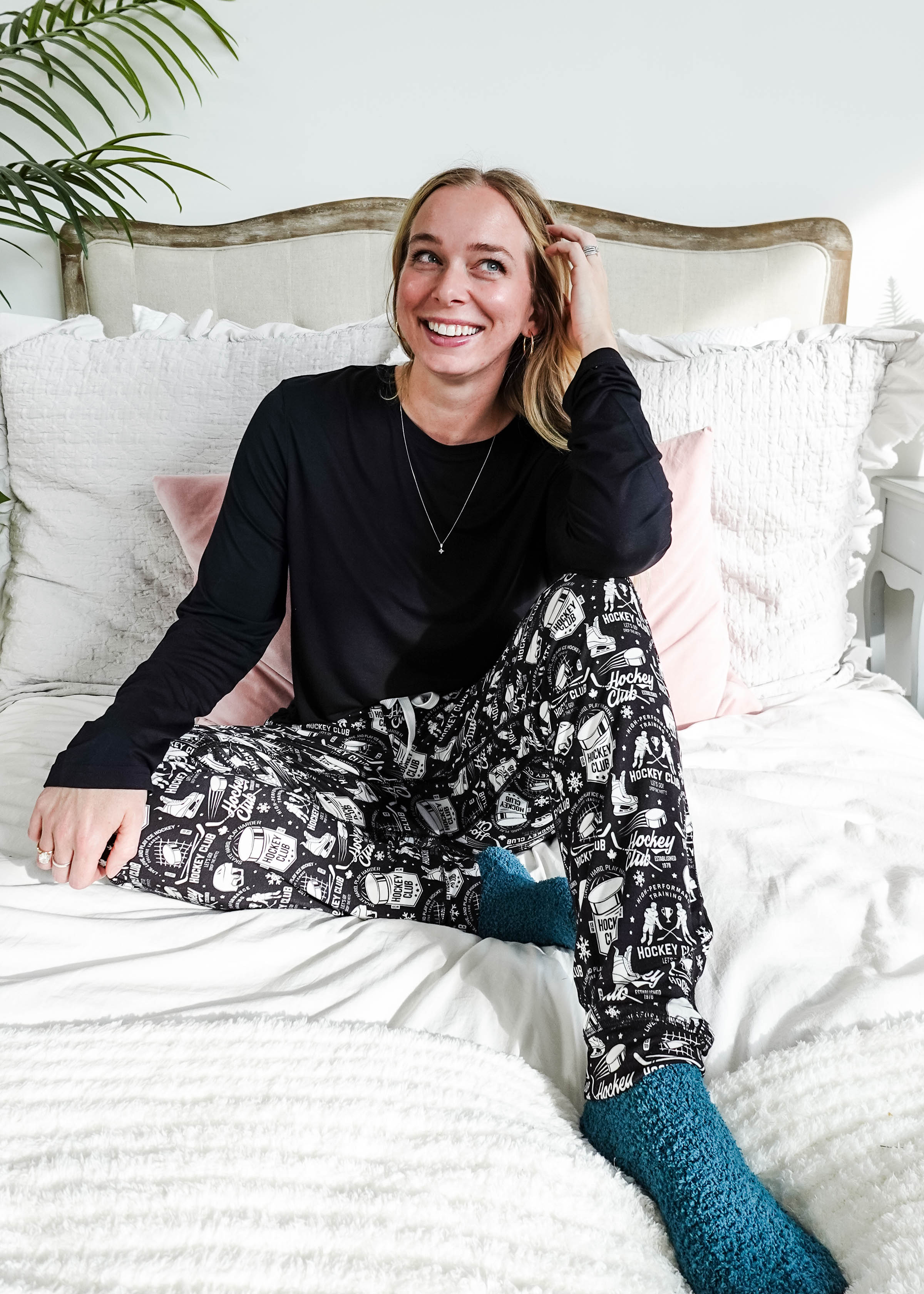 He Scores Hockey Print Unisex Bamboo Jogger worn by a smiling woman sitting on a bed with cozy decor.