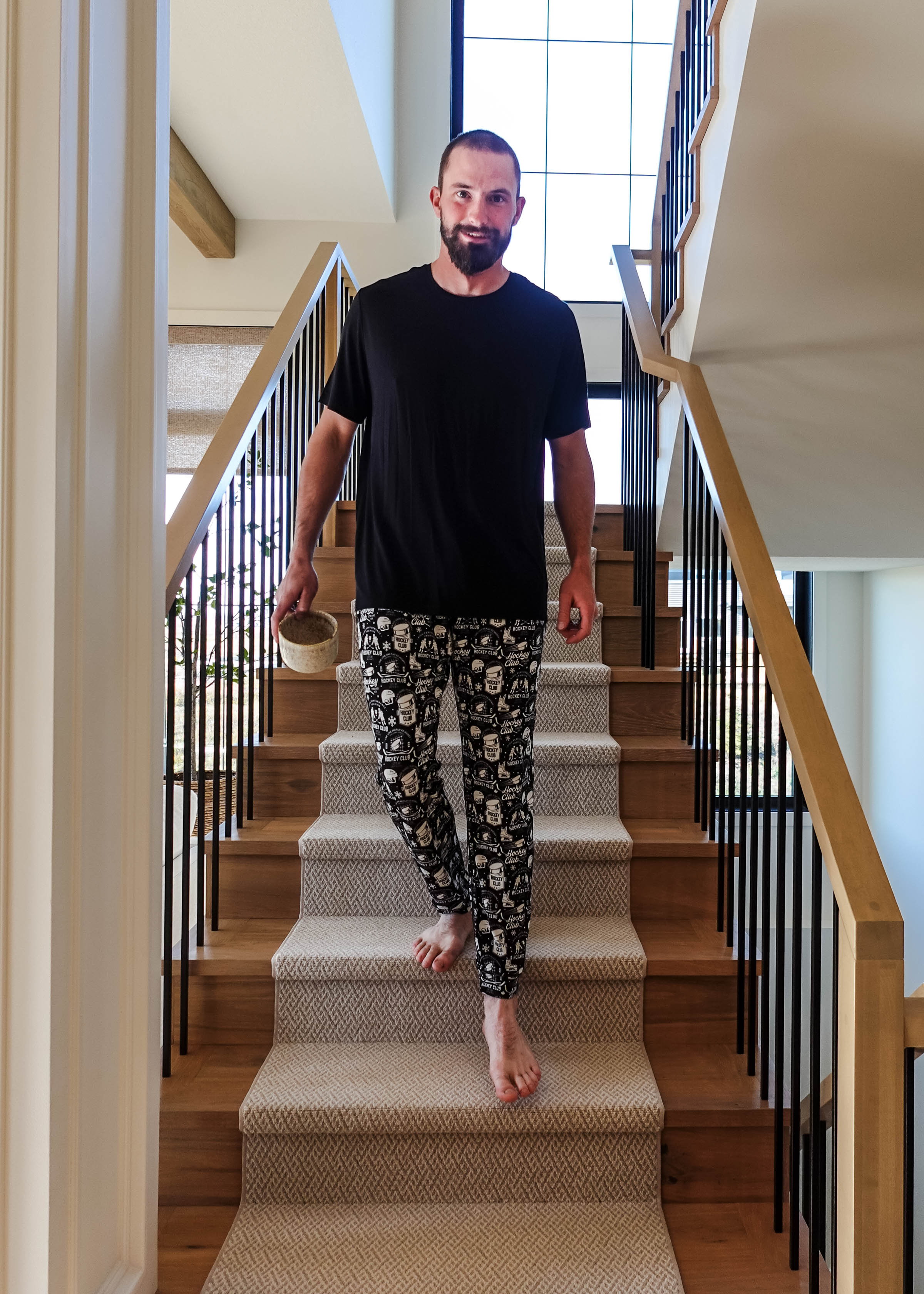 Man in He Scores Hockey Print Unisex Bamboo Jogger descending stairs with a drink in hand.