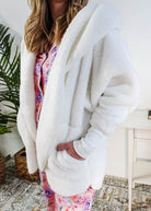 Essential Hooded Fluffy Cozy Cardigan with Pockets worn by a woman with floral pajamas in a cozy bedroom setting showing close up of the texture of the sweater