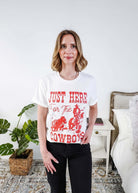 Woman wearing a white t-shirt with red text saying Just here for the cowboys in a bedroom setting