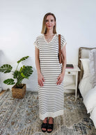Woman in a striped dress standing in a bedroom with a plant and nightstand.
