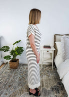 Woman in a striped  black and white knit dress standing in a bedroom with a plant and bed in the background