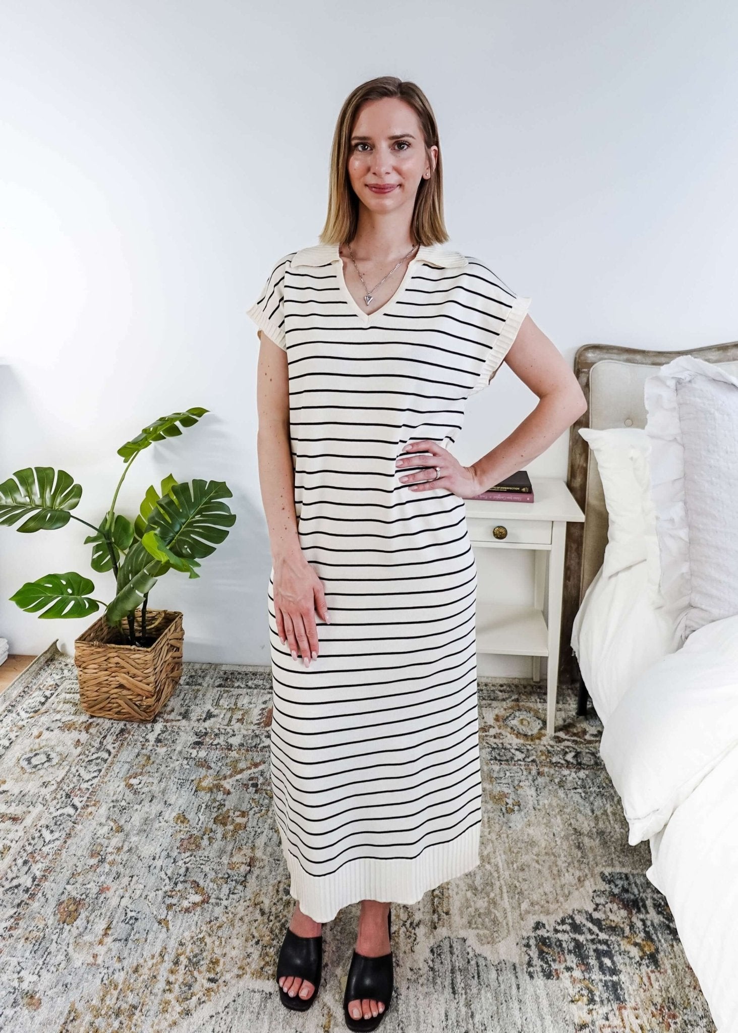 Woman wearing a black and white striped dress in a room with a plant and bed.