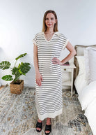 Woman wearing a black and white striped dress in a room with a plant and bed.