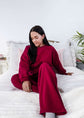 Woman in a red sweatsuit sitting on a bed in a bright room with white walls and a plant.