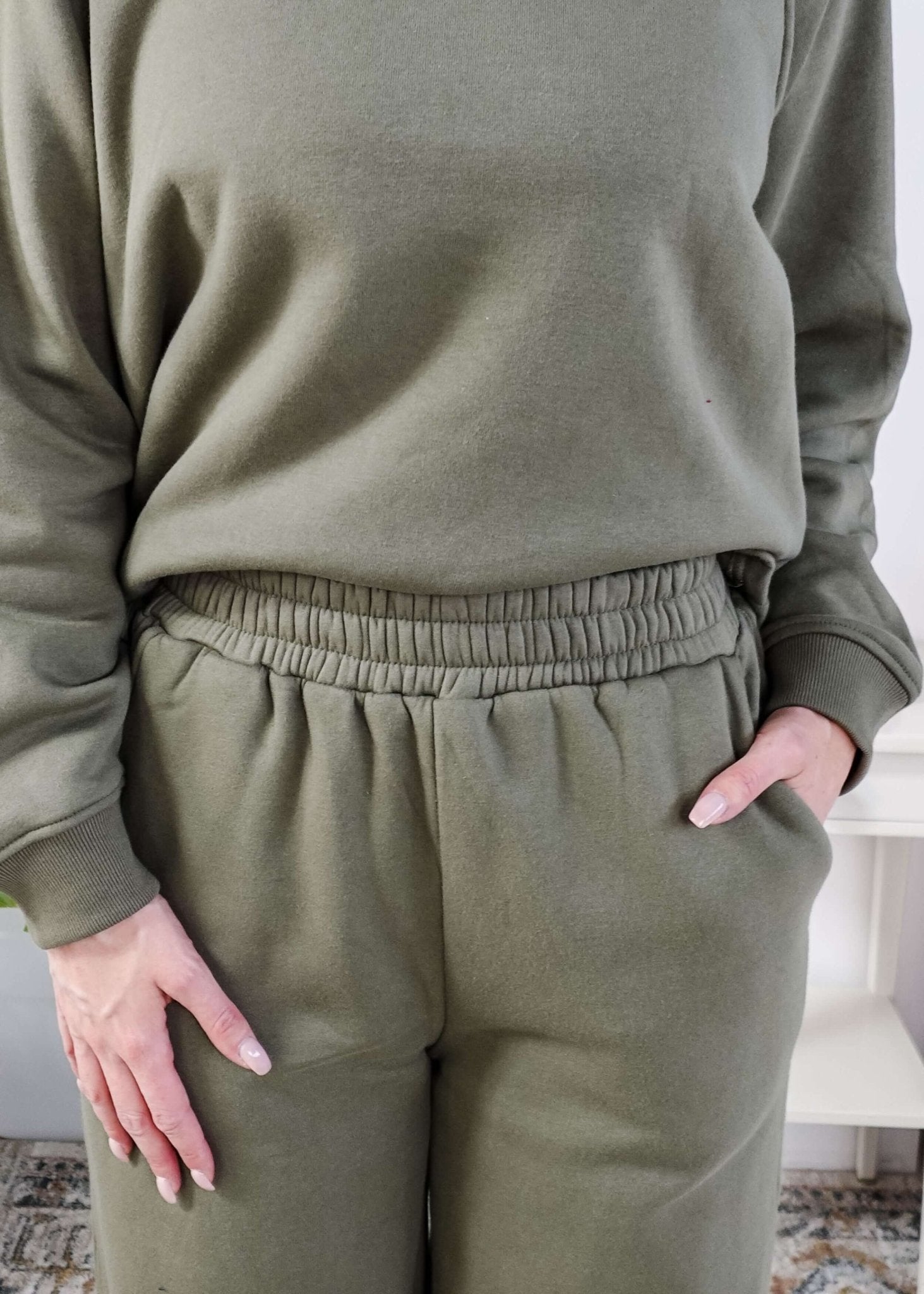 Person wearing a green sweatsuit with hands in pockets indoors.